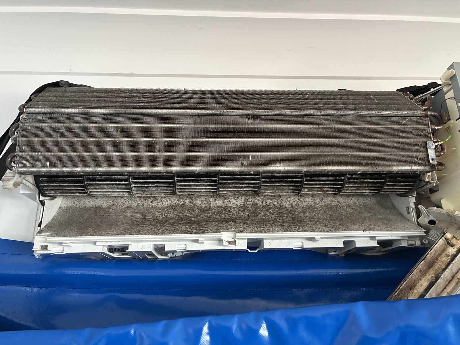 Air conditioner opened for cleaning, showing the evaporator coil and barrel fan caked in dark dust and grime
